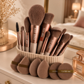 Professional makeup brush set with rose gold handles and beauty blending sponges displayed on a bedroom dresser vanity.